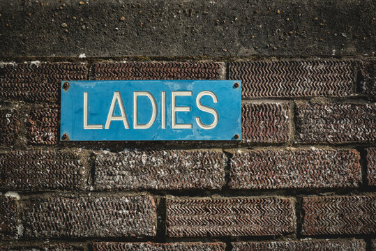 Blue sign 'Ladies' on a brick wall; Southwold, Suffolk, England
