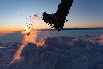 Man climbs a mountain peak in winter during sunrise. A shoe with spikes on - crampons. Winter in...