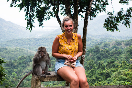 Tropical monkey eating with woman on a bench in the jungle