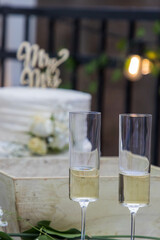 Two filled champagned glasses sit on a table in front of a wedding cake with with roses.