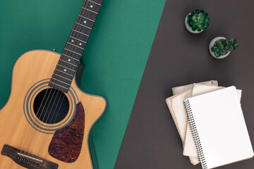 Acoustic guitar and empty notebook on a colored background, top view.