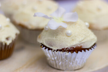 A white frosted chocolate cupcake with  a white flower lays on a wooden table.