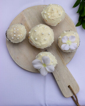 Five white cupcakes lay on a wooden tray on a table with a white table cloth. 