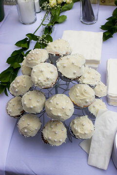 White frosted chocolate cupcakes arranged on a stand on a table with a white table cloth.