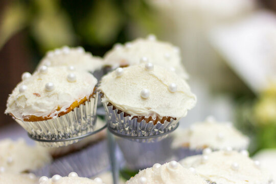 Wedding cupcakes with white frosting in a stand on a white table.