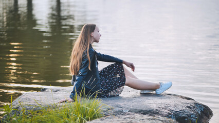 A girl sits by the lake on a rock.
