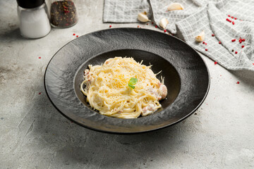 Spaghetti Carbonara with bacon on black plate on grey table