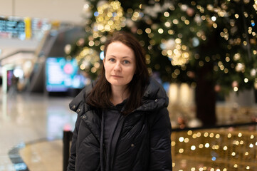 Fototapeta premium Portrait of a beautiful woman on the background of a Christmas tree with bright lights gerlant. Beautiful multicolored bokeh in the background
