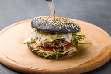 Black Burger with meat, aragula and vegetables on the board on grey table