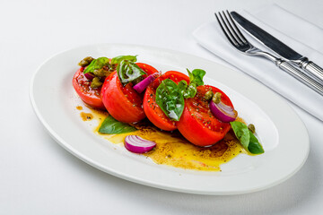 Tomato salad with red onion and basil on white plate