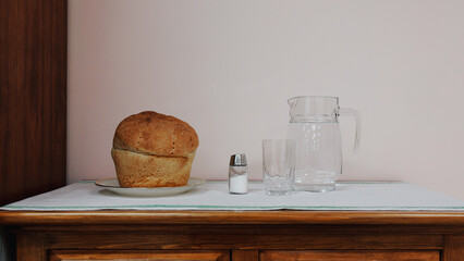 A small still life freshly baked bread, salt, a glass and a decanter are on the table.
