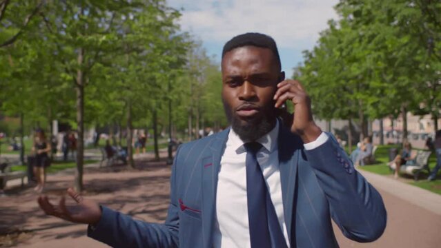 Angry African-American businessman have phone call outdoors. Realtime