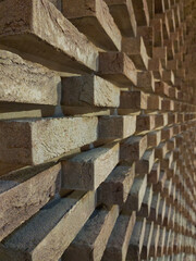A long brick wall in perspective. Bricks are laid out in a pattern with different depths of brick laying. The distant background is blurred