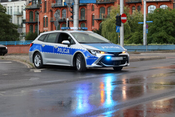 Radiowóz policji polskiej drogówki wieczorem w deszczu na mieście.