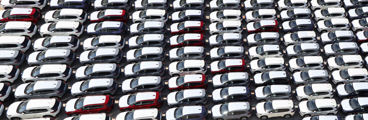 Aerial view of new cars stock at factory parking lot. Above view many cars parked in a row. Automotive industry. Logistics and supply chain business. Import or export new cars at warehouse near port.
