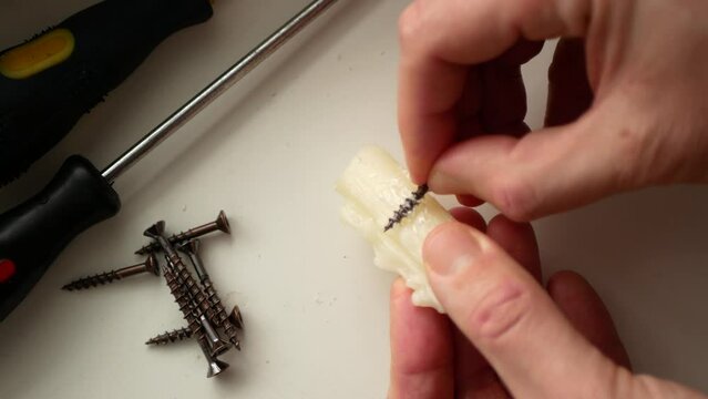 Woodworker is rubbing some candle wax on the screws before driving them into wood joints. Wax coating screws, selective focus. Concept of crafty idea or life hack