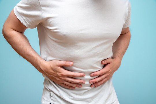 Man in white shirt holding his stomack out of pain.