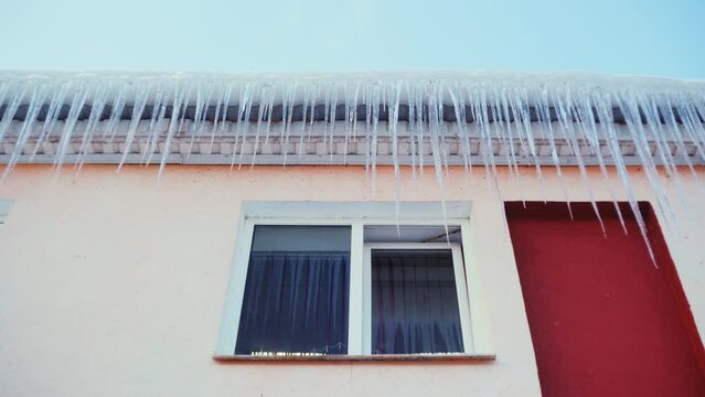 Large icicles hang from the overhang of the roof of the building. Falling ice- winter hazard for passersby