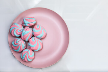 Colorful fluffy marshmallows on a pink dish on a glossy white background