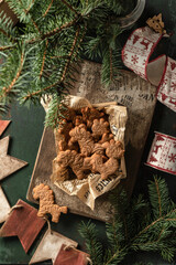 Christmas cookies or gingerbreads of patterned animal shapes on in wooden box on green wooden table. Xmas or new year rustic composition with fir tree and festive decor, top view