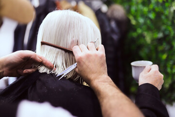 hairdresser's hands with scissors and comb cutting hair of older woman with white hair