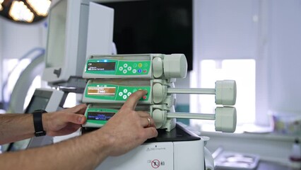 Male hands press and hold the buttons of a syringe infusion pump. The movable parts of the device starting to move.