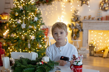 Cute preschool child, blond boy, making advent wreat at home in decorated Christmas room