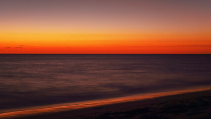 Fototapeta na wymiar Vibrant orange red sky reflecting in calm ocean after sunset. Minimal landscape photo with space for text
