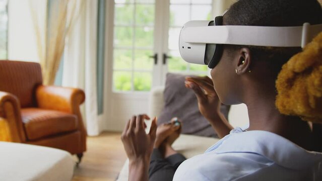 Woman relaxing lying on sofa at home wearing VR headset and interacting with AR technology - shot in slow motion