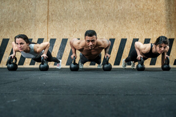 Latin workout group of two women and a fitness man performing plank on Russian weight facing the camera.