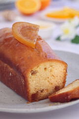 A whole orange cake topped with its sliced candied in a black plate with its fruits and with a cut and sliced piece, it's a moist and soft sweet cake with entire orange used