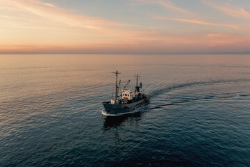 Fishing boat catching fish at sunset aerial view from drone. Small fishing trawler ship on sea surface.