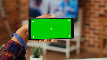 Young adult holding telephone with horizontal greenscreen, analyzing blank chroma key template and...