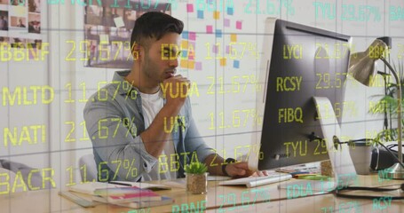 A man is working at a desk in an office, looking at a computer screen and writing