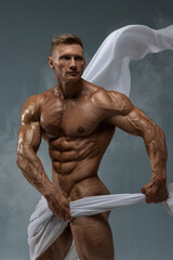 Athletic strong man posing in a studio white cloth in an original way