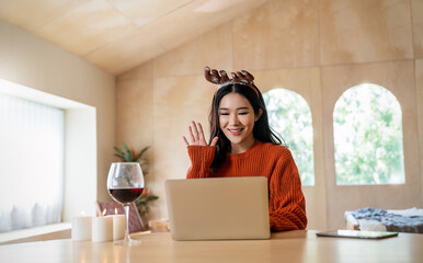 Portrait of beautiful business asian woman live online say hi on computer. Freelance online marketing, young happy girl video call on laptop toasting with red wine celebrating Christmas alone at home.