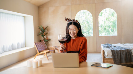 Fototapeta na wymiar Portrait of beautiful business asian woman live online say hi on computer. Freelance online marketing, young happy girl video call on laptop toasting with red wine celebrating Christmas alone at home.