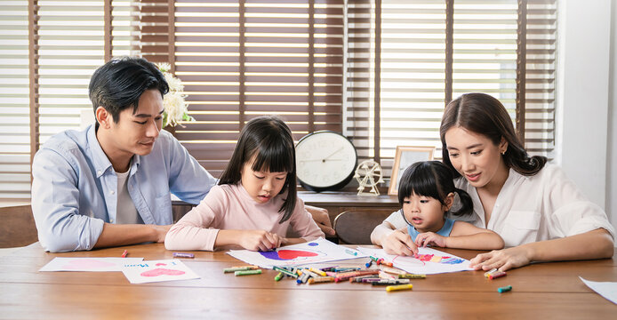 Portrait of Asian Mother Father teaching daughters learn to write color on paper book, Asian parents helping little girl do homework. Education art work love together home school family day concept