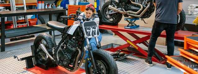 Cercles muraux Moto Female mechanic repairing custom motorcycle on factory
