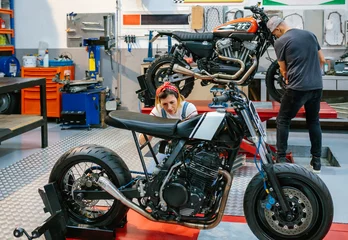 Photo sur Plexiglas Moto Mechanic female checking custom motorcycle while her colleague adjusting motorbike wheel over platform on garage