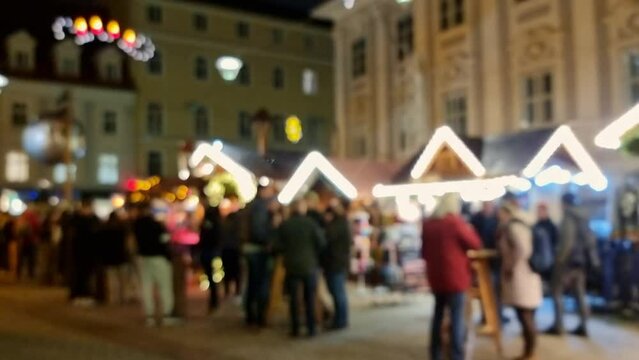 Blurred silhouettes of people at a Christmas market with beautiful decorations and wooden little houses, at night, magical holidays atmosphere in the city center of Graz, Styria region, Austria