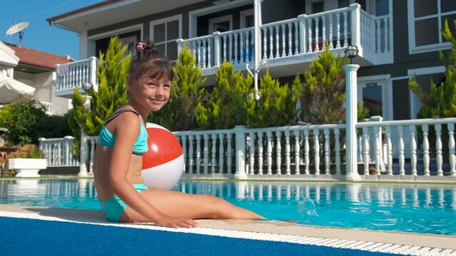 Child with rainbow ball by pool. A cute little girl relax under sun wuth her inflatable ball by home pool under sun.