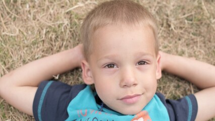 Little Happy Serious and Thoughtful Child Boy Laying on Yellow Lawn Dry Grass Hay in Park. Summer Time, Nature, Dreams, Lifestyle Country life farm village. Smilling Face Close up Looking at Camera