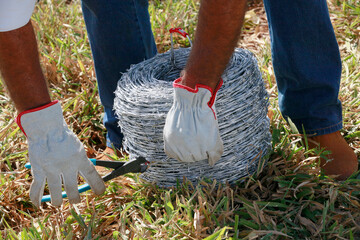 A man s hands manipulate rolls of barbed wire with pliers