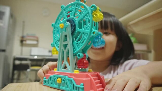 Five-year old Chinese Indonesian girl playing with plastic ferris wheel toy in a living room setting. Static shot, low angle. Indoor.