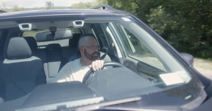 A bald man peacefully driving a Subaru on a rural road