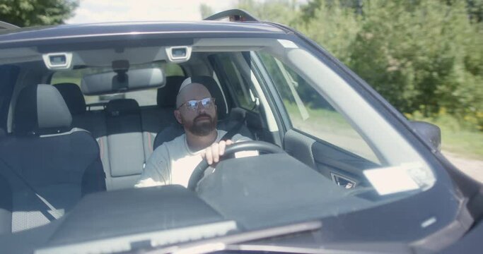 A bearded man with glasses drives on a rural road, turns left and pulls over.