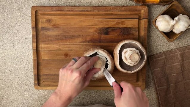 Video. The cook cleans mushrooms in the home kitchen, on a cutting board. Nearby lies garlic and a knife. The process of preparing mouth-watering mushroom dishes. Recipes.