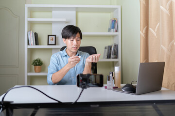 Young adult Asian beauty video blogger man filming, online live streaming his video blog about male cosmetic, male skincare. Guy looking camera to show new skin care for men product, teaching make up.