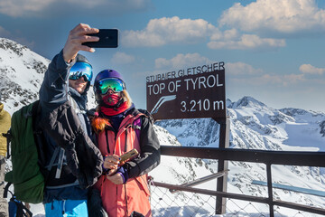 Happy skier and snowboarder couple taking a selfie photo on top of Tyrol, Austria